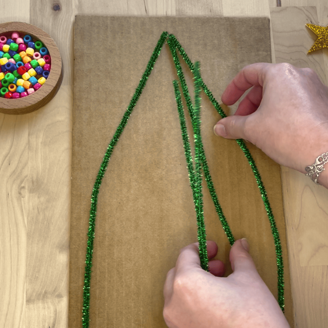 Maestra pegando limpiapipas verde simulando un árbol de navidad